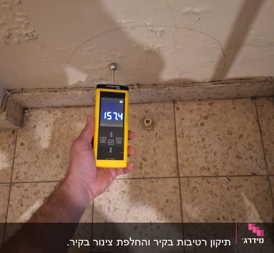 מד לחות צמוד לקיר עם סדקים, יד מחזיקה את המכשיר
